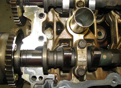 Demontáž vačkových hřídelů - Pod víkem ložiska vačkové hřídele jsou viditelné známky provozu motoru s omezenou funkčností mazání. Odřená plocha ložiskové části „vačky“ má matný povrch.  